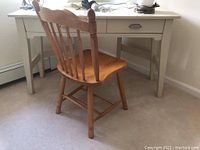 Two drawer light-colored desk with metal handles paired with wooden chair with spindle backrest, natural finish, and contoured seat.