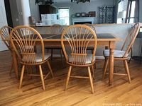 Six wooden dining chairs around a wooden dining table on a hardwood floor, showing overall condition and style.