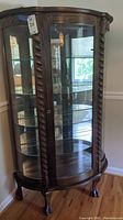 Full front view of antique wooden curio cabinet with curved glass panels and claw feet, showing internal glass shelves and front lock.
