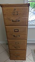 Front view of four-drawer file cabinet showing wood grain laminate drawers, metal handles, and lock with key on top drawer