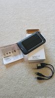 Solar charger device on top of its packaging with accompanying USB cables and instruction manual, black solar panel surface visible.