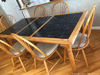 Photo of wooden kitchen table with black tile top and six matching chairs around it, showing the tabletop and chair arrangement