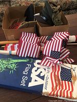 Boxed military hats with multiple small American flags and large American flag box on a wooden table.