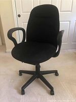 Front view of black fabric office chair with cushioned seat and backrest, curved armrests, and wheeled base.