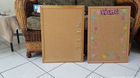 Two corkboards shown side by side on floor; one plain wood framed with magnets, one decorated with colorful flowers and name.