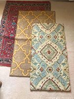 Top-down photo showing all three rugs partially overlapping on a beige carpet. Left rug is red with floral pattern, middle is beige with yellow lattice design, right is blue runner with cream and burgundy diamond motifs.