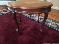 Full view of the oval solid wood side table showing tabletop inlay, wood finish, and cabriole legs with claw feet.