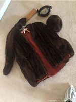 Waist length mink fur stole laid flat with reddish-brown lining visible, a round mink fur hat, and a mink fur neck wrap with bow fastening visible on carpet.