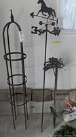 Photo showing all three items: the domed metal plant trellis, the weather vane with horse figure, and the metal hose holder against garage wall.