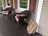 Wide view showing two wicker chairs with cushions and the matching wicker table between them, plus additional cushions on the floor.