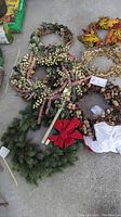 Photo showing multiple wreaths including artificial greenery with a red bow, berry-covered twig wreaths, natural acorn and twig wreath, and floral accents.