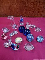 Full set of 17 assorted glass animals, decorative balls, and other home decor items, mostly clear with some colored blue glass pieces, displayed on a red surface.