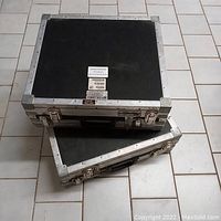 Two Wilson shipping travel tradeshow cases stacked on tile floor, showing black bodies with metal edges and latches.