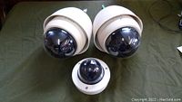 Photo of three Bosch dome security cameras on a green surface: two larger vandal mini domes with sun shields and one smaller dome camera.