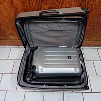 Open large soft-sided suitcase showing inside compartments and silver hard-shell carry-on suitcase inside.