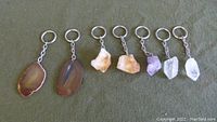 Seven assorted natural geode keychains laid out in a row on a green surface showing both polished and rough stones attached to key rings.