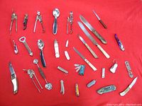 Top down view of all 30 assorted small hand tools including knives, nail clippers, spoons, and multitools arranged on red fabric