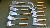 Full view of 12-piece cooking utensils laid out with wooden handles and metal heads, along with metal wall rack with hooks for hanging.