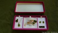 Full jewelry set displayed in open red box, showing chain with green pendant, brooch, and earrings laid out on white padding.