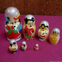 Full view of all 7-piece nesting dolls displayed in descending size order with different Disney characters hand-painted on each doll.