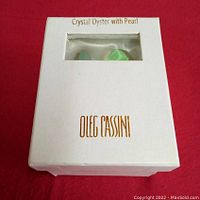 White box with gold Oleg Cassini logo and 'Crystal Oyster with Pearl' text, small window showing iridescent crystal oyster inside.