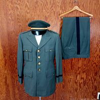 Full view of jacket, pants, and service cap placed on top of the jacket on hanger against wood background.