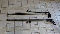 Two pairs of black SportCamZ hiking poles laid out on tile floor with removable snow baskets placed near poles.