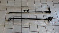 Two pairs of black hiking poles laid out parallel on a tiled floor with rubber tips beside them