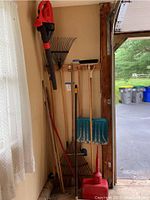 Wide view of electric leaf blower and various garden tools including rakes, shovel, broom, and edger hung on the wall of a garage corner.