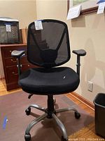 Front view of black mesh adjustable desk chair showing padded seat and armrests in a home office setting.