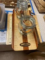 Photo of two artisan wooden cutting boards placed horizontally on table with ruler for scale, showing glossy finish and wood grain detail, along with two European glass jars having metal clasp lids.