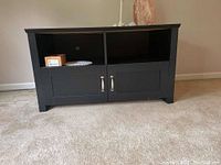 Front view of the black TV cabinet showing two doors with pewter-colored handles and two open cubbies above.