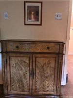 Front full view of wooden chest with painted foliage detail under artwork on wall