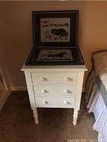 Full view of vintage cream colored end table with two framed prints on top showing a black cat and a black horse.