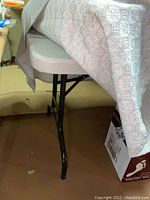 Side view of plastic and metal folding table with beige patterned tablecloth draped over it