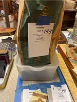 Photo of a white plastic container holding a brown paper bag filled with packaged furniture pads and sliders