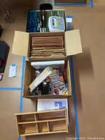 Overview of two cardboard boxes containing file folders, desk organizers, stationery, and a Brother P-Touch label maker on top.