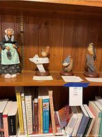 Three limited edition bird sculptures and a vintage figurine on wooden shelves with books below, showing variety of items in the lot.