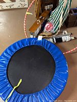 Blue mini trampoline with protective blue cover and yellow strap, shown from top angle.