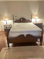 Front view of the queen-size vintage cherry wood bed frame with mattress and topper. Two lamps and nightstands are visible on either side.