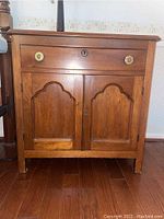 Front view of small vintage wooden chest showing drawer and double doors with decorative ceramic knobs.