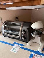 Side view of the toaster oven and citrus press together on a kitchen counter, showing overall size and condition.