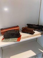 Photo showing three Lionel train cars including a black locomotive, black tender, and brown caboose with box and instruction manuals on a white shelf.
