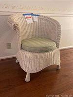Side view of white wicker chair showing curved back and arm with braided detail and circular upholstered seat.