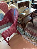 Red wicker chair and oak wood table placed on a multicolor braided rug in basement setting.