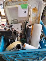 View of contents inside blue milk crate showing caulking dispensers, rollers, tape rolls, and some brushes