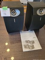 Pair of Bose 201 bookshelf speakers in black on table with user manual beneath them. Both speakers show front view with fabric grille and visible tweeter.