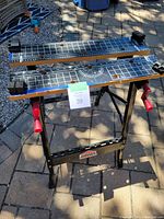 Front-top perspective showing the printed grid tabletop with measurement rulers and vise clamps with red handles, the Jobmate brand label on the metal frame.