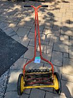 Full view of red and yellow manual push reel lawn mower on stone patio, showing handle and wheels