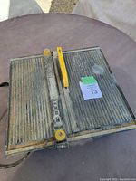 Top view of Mastercraft wet tile saw showing the cutting surface with ridges and adjustable yellow guide bar, signs of wear and some dirt.
